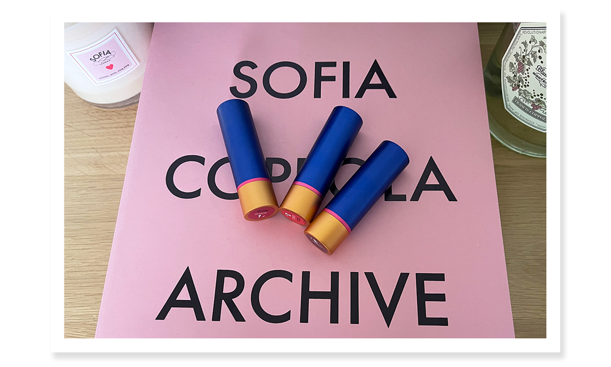 Showing a Sofia Coppola candle, her Archive book, three tinted lip balms with their caps on, and a bottle of Sofia Blanc de Blanc